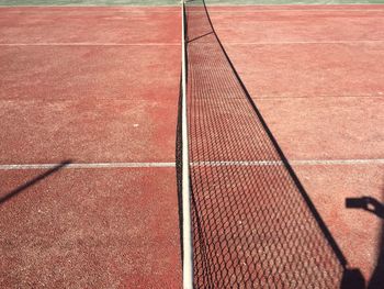 High angle view of net with shadow on brown tennis court