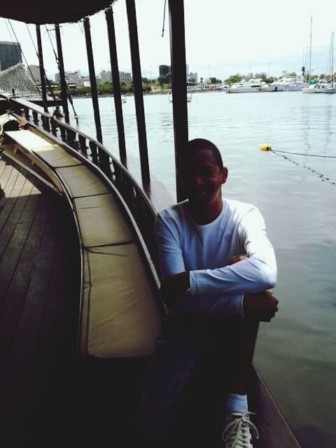 water, casual clothing, lifestyles, leisure activity, person, nautical vessel, railing, sitting, built structure, river, full length, young adult, standing, architecture, rear view, day, boat, young men