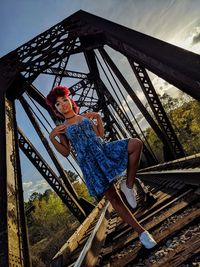 Portrait of woman sitting on railing against sky