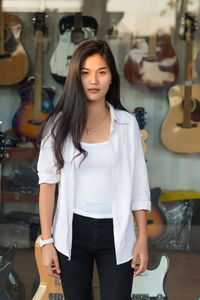 Portrait of young woman standing against guitar store