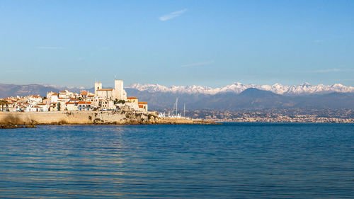 View of sea with snowcapped mountains in background against blue sky