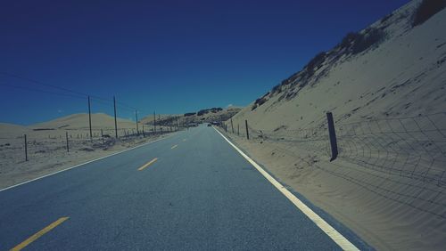 Road by snowcapped mountains against clear blue sky