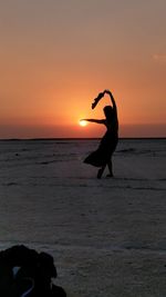 Silhouette woman on beach against sky during sunset