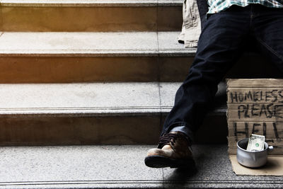 Low section of homeless man sitting with sign on steps