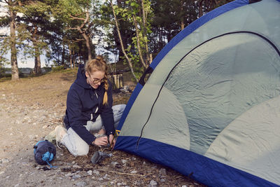 Young woman kneeling while setting up tent at campsite