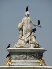 Birds perching on statue against sky