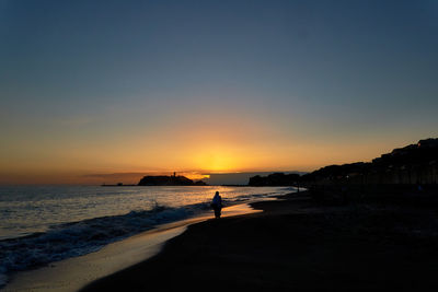 Silhouette people standing on beach against clear sky during sunset