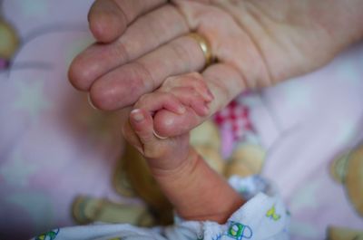 Cropped hands of mother and newborn on bed