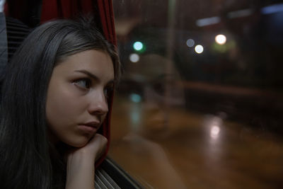 Close-up of young woman looking through train window at night