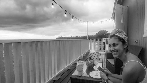 Portrait of young woman on railing against sky