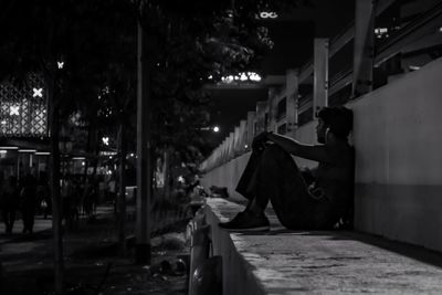 Side view of man sitting on sidewalk in city