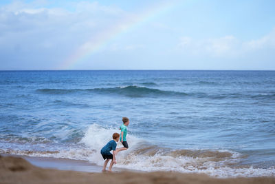 Young boys playing in the waves with a rainbow over the ocean on ka'anapali beach in hawaii. 