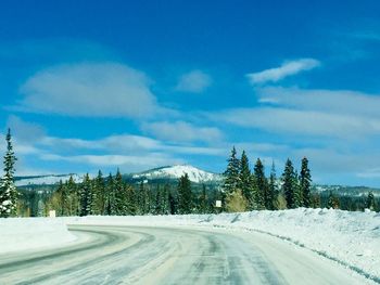 Snow covered road by trees against sky