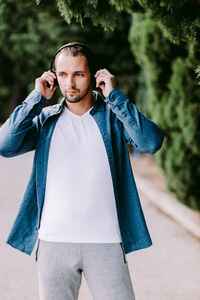 Handsome man listening music over headphones while standing in park