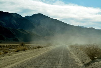 Empty road leading towards mountains against sky