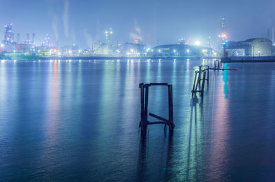 Scenic view of sea against illuminated industrial buildings