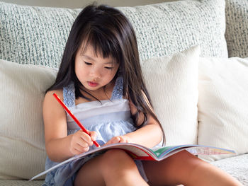 Girl writing in book while sitting on sofa at home
