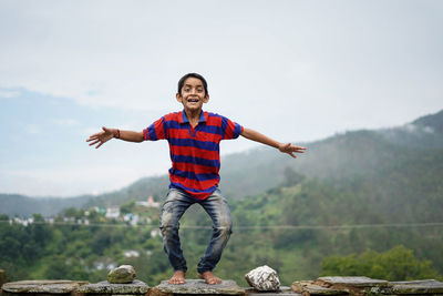 Full length of smiling young man standing on mountain against sky