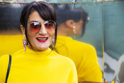 Fashionable mature woman wearing yellow top and sunglasses in city