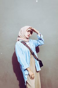 Woman in hijab shielding eyes while standing against wall