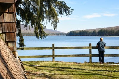 Rear view of man standing by lake against sky