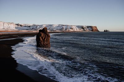 Rear view of horse on rock by sea against clear sky