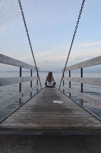 Rear view of woman sitting on jetty over sea against sky