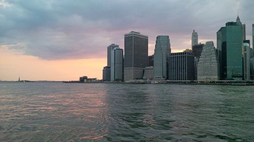 Sea by buildings against sky during sunset