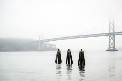 People on suspension bridge over river against sky