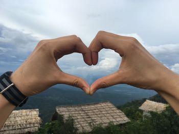 Close-up of hand holding heart shape against sky
