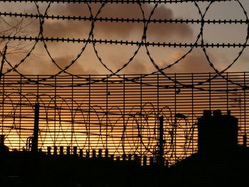 Silhouette chainlink fence against sky during sunset