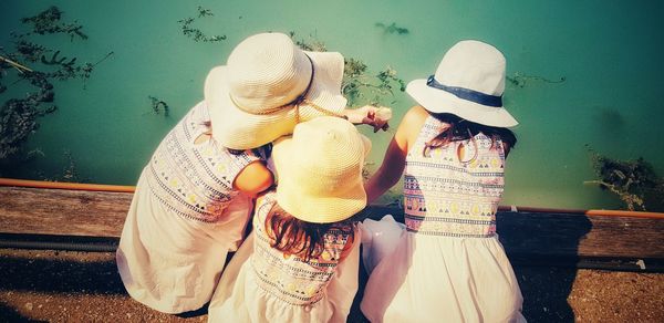 High angle view of girls wearing hat crouching on pier over lake