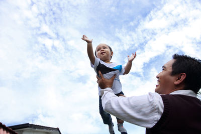 Low angle view of father and son playing against sky