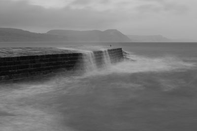 Long exposure of the waves crashing up against the pier at lyme regis in dorset in black and white