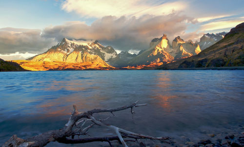 Scenic view of lake by snowcapped mountains against sky during sunset