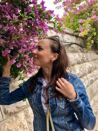 Smiling woman in denim jacket touching flowering plant