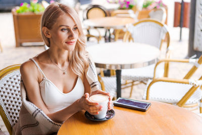 Beautiful young woman in warm plaid in an outdoor cafe at table drinking