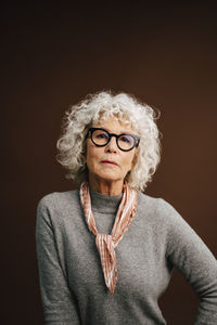 Portrait of elderly woman wearing eyeglasses over brown background