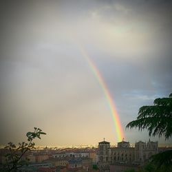 Rainbow over city against cloudy sky