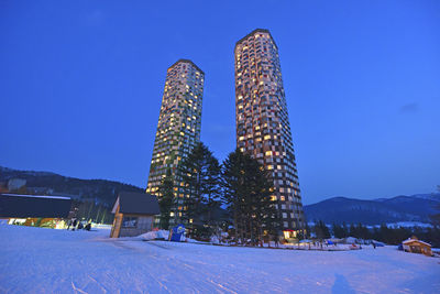 Illuminated snow covered buildings against clear blue sky