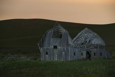 Abandoned barn on grassy field against clear sky during sunset