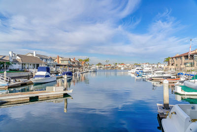 Boats moored in canal by buildings against blue sky