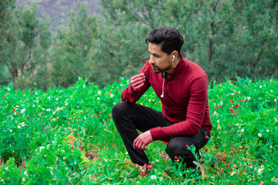 Young man smelling flowers while crouching on field in park