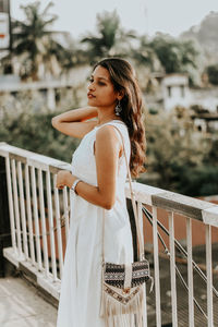 Side view of young woman standing against railing