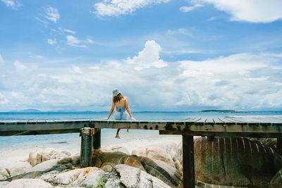 Rear view of woman standing on rock by sea against sky