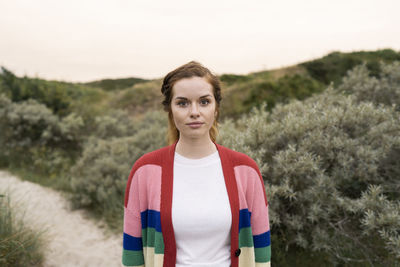 Beautiful young woman wearing multi colored cardigan sweater standing in meadow