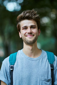 Portrait of young man with backpack standing at park