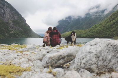 People crouching by dog against mountain