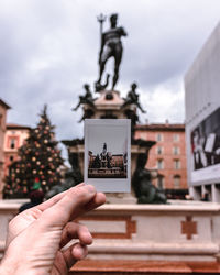 Hand holding statue against buildings in city