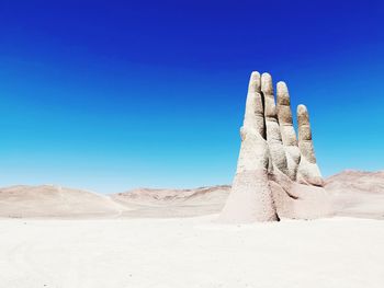 Sculpture of hand in desert against clear blue sky